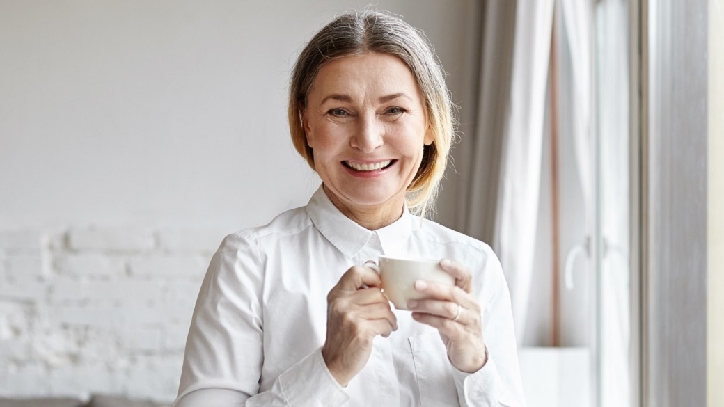 Lächelnde Frau mit Tasse in der Hand im Wohnzimmer